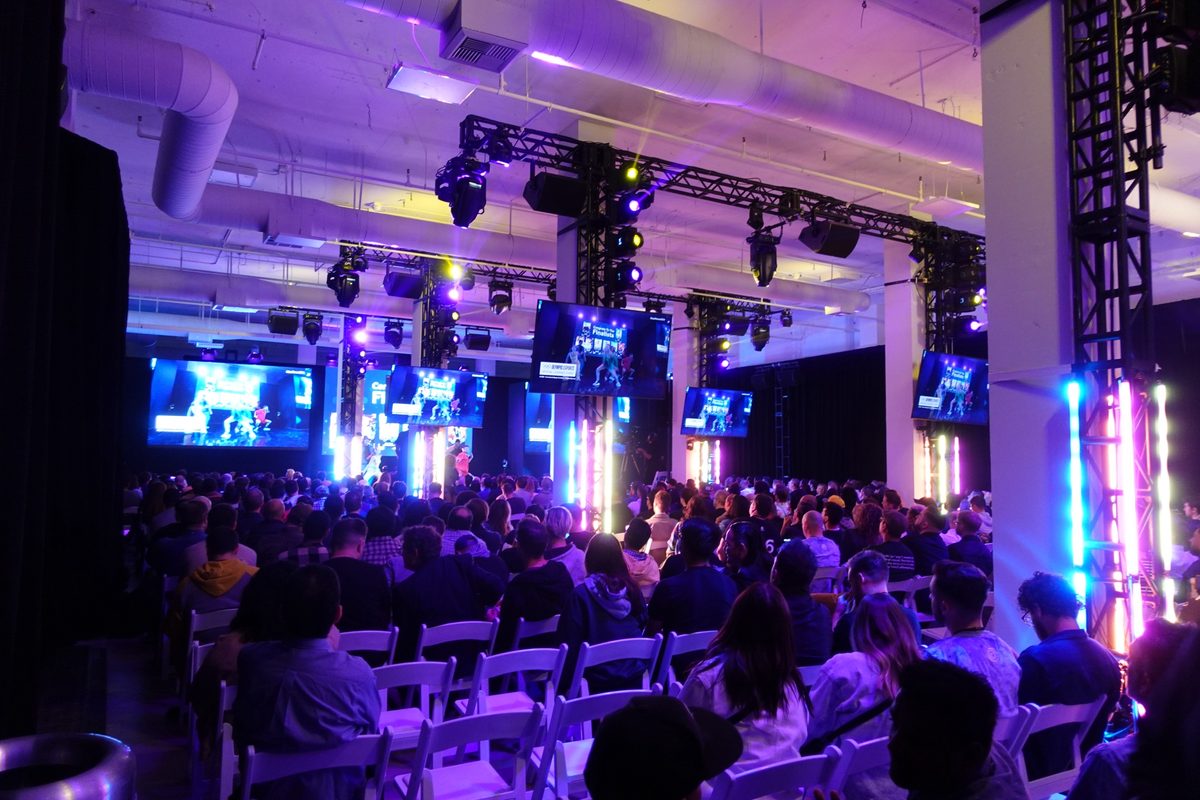 A seated audience facing a lit stage and screens