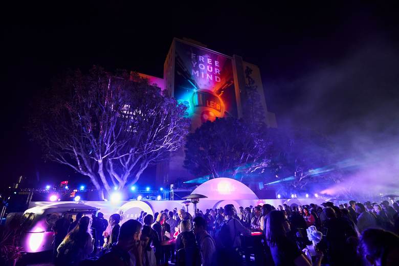 A crowd at a night performance with a projection on the building